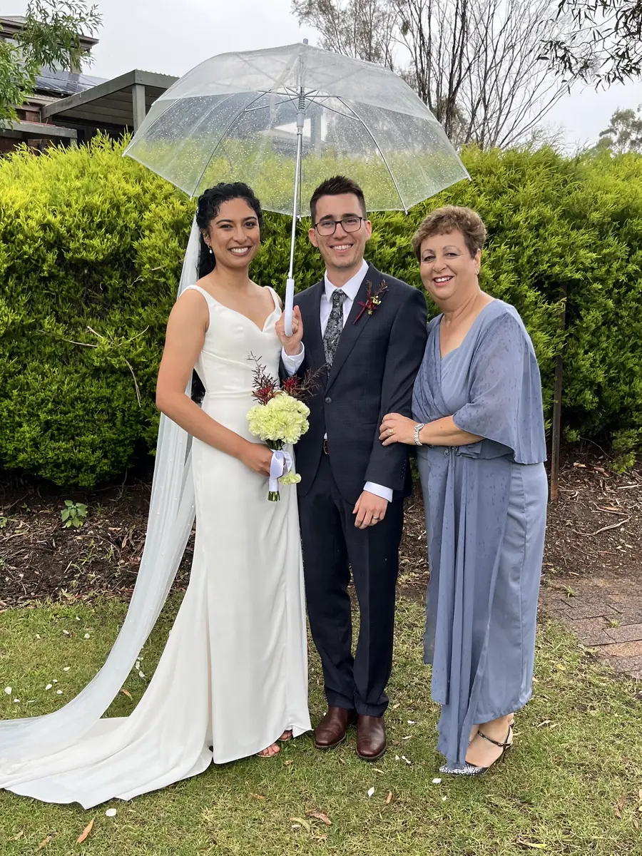 Josie with a bride and groom sheltering under a clear umbrella in a garden