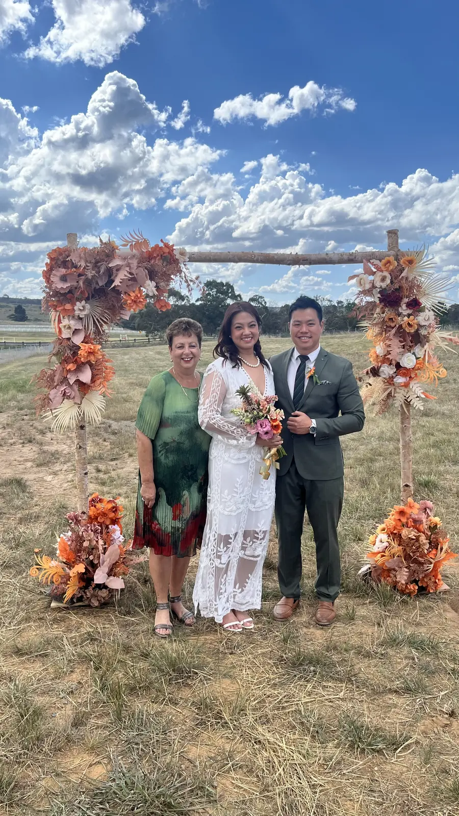 Josie with a couple in front of a dried-flower arch in an open paddock